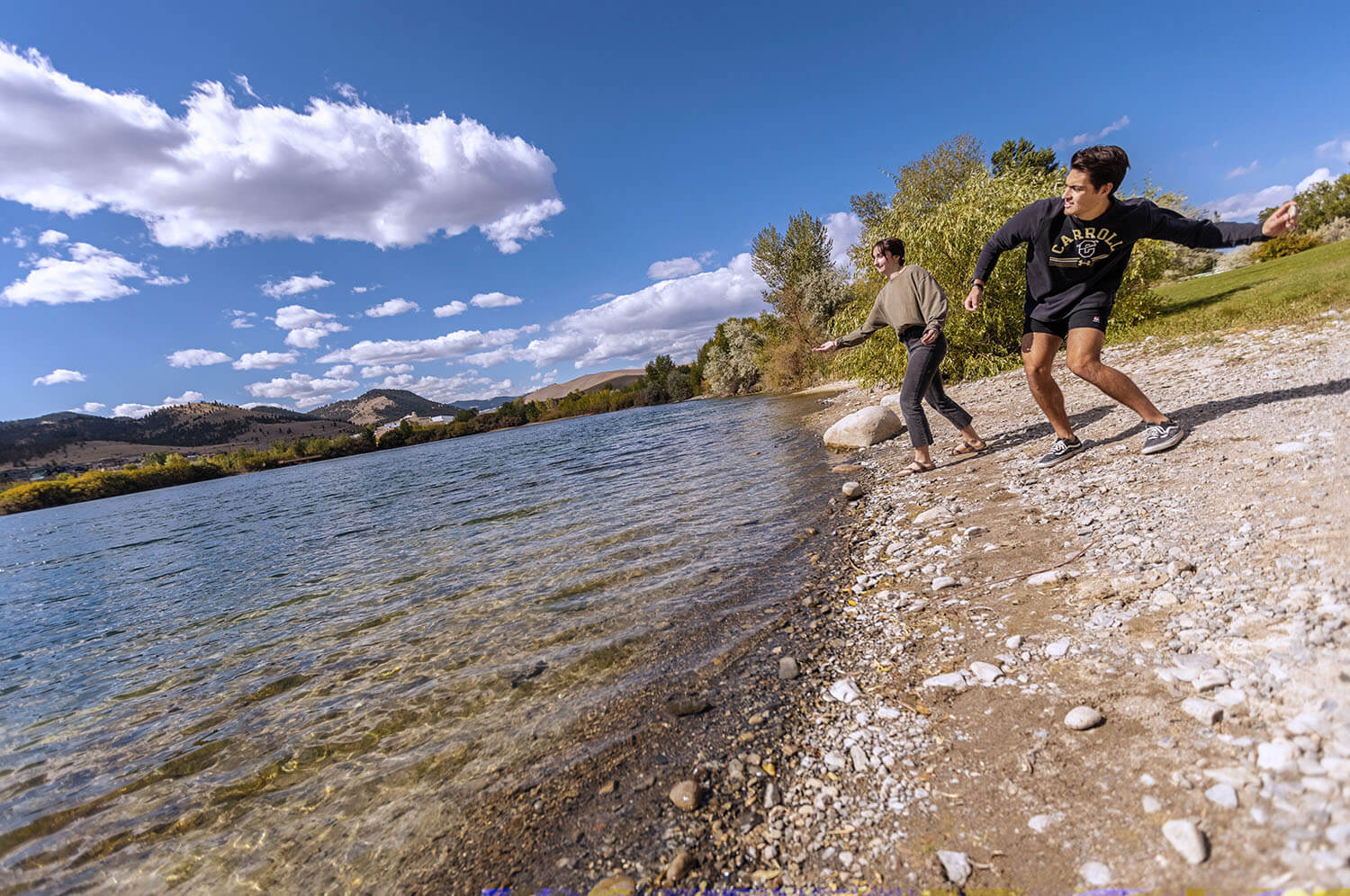 Two students skipping rocks against a perfectly blue sky and clear river