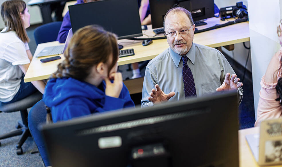 Faculty member sitting at a computer assisting a student