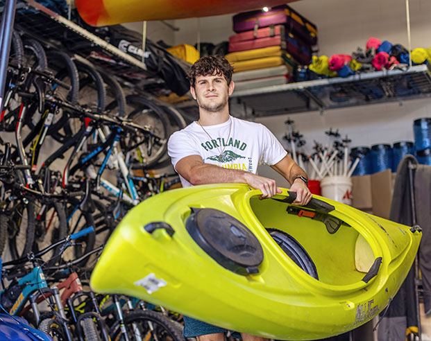 Student carrying a green kayak out of an equipment room