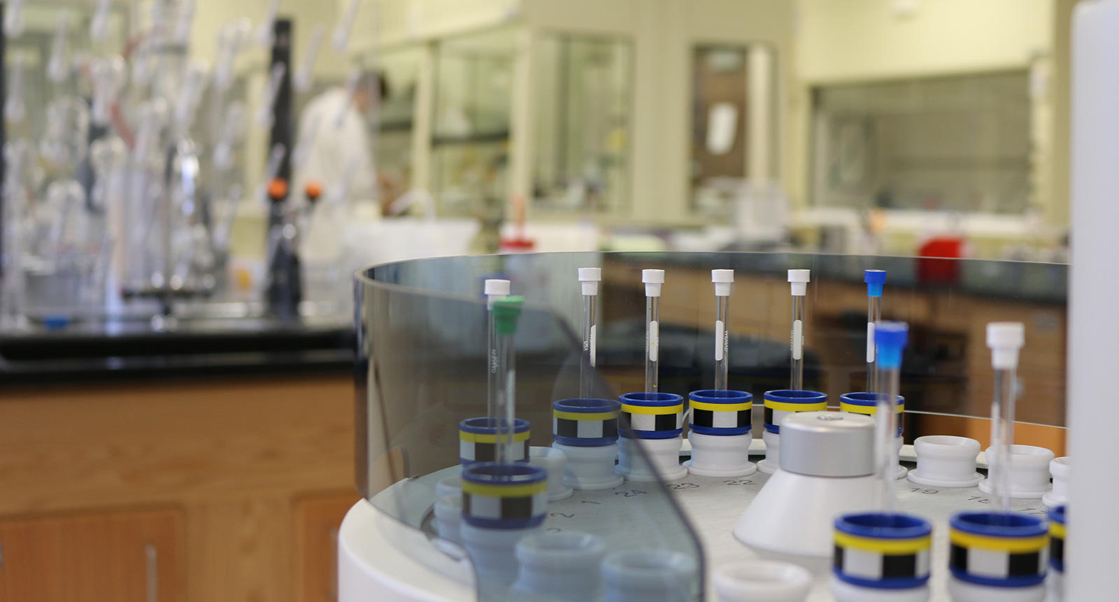 Integrated lab instruments and work tables with a blurred person in a lab coat in the background