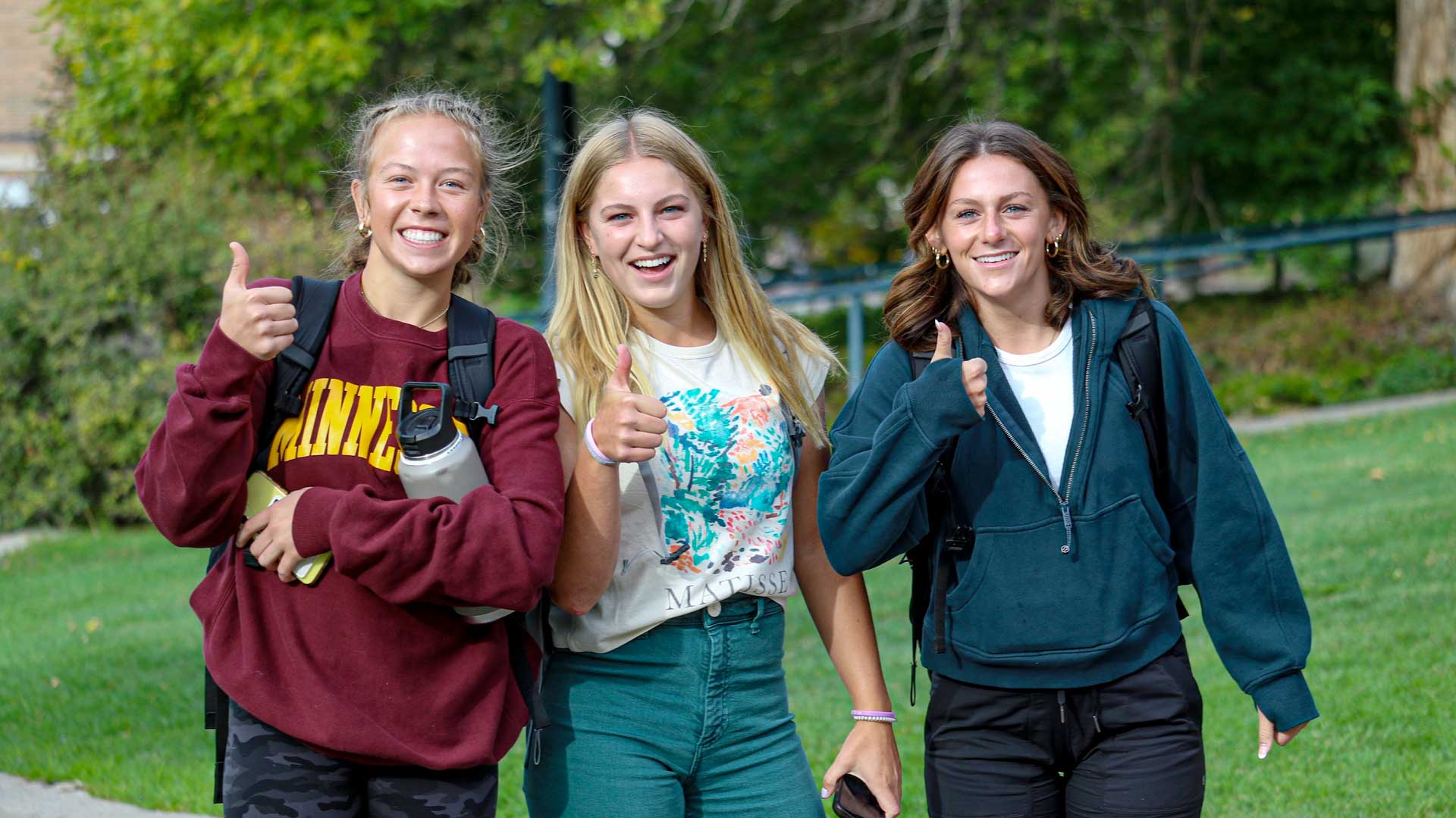 Three female students outside - thumbs up