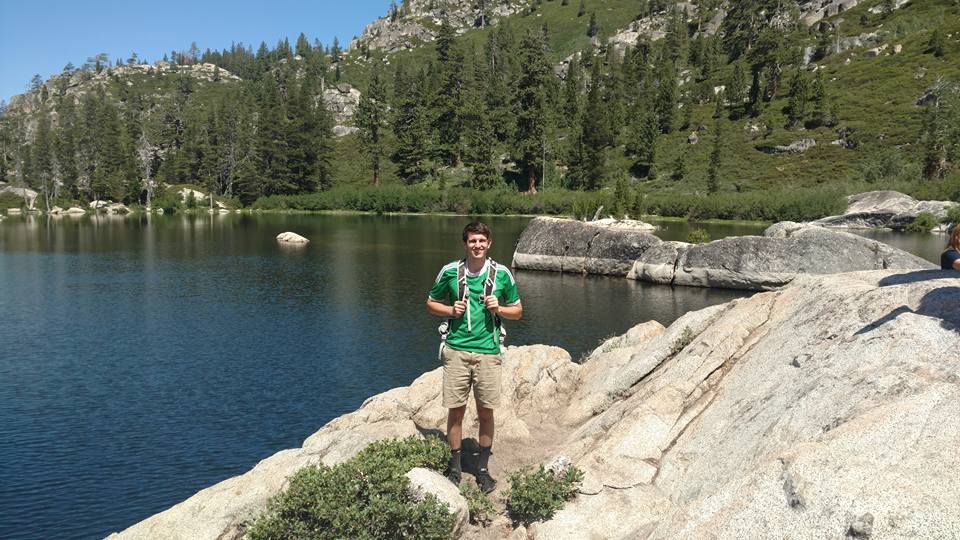 Tyler Zimmer standing on a rock by a mountain lake