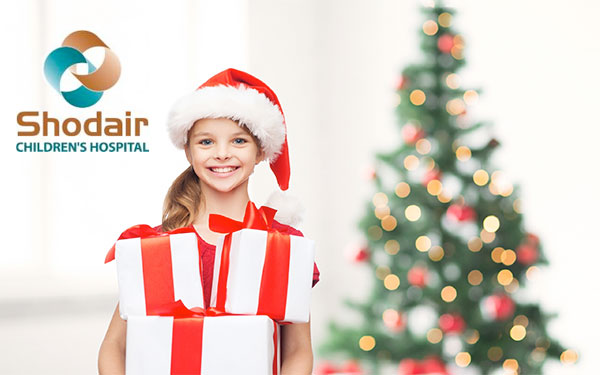 Young girl in a Santa hat holding red and white gifts with a Christmas tree in the background