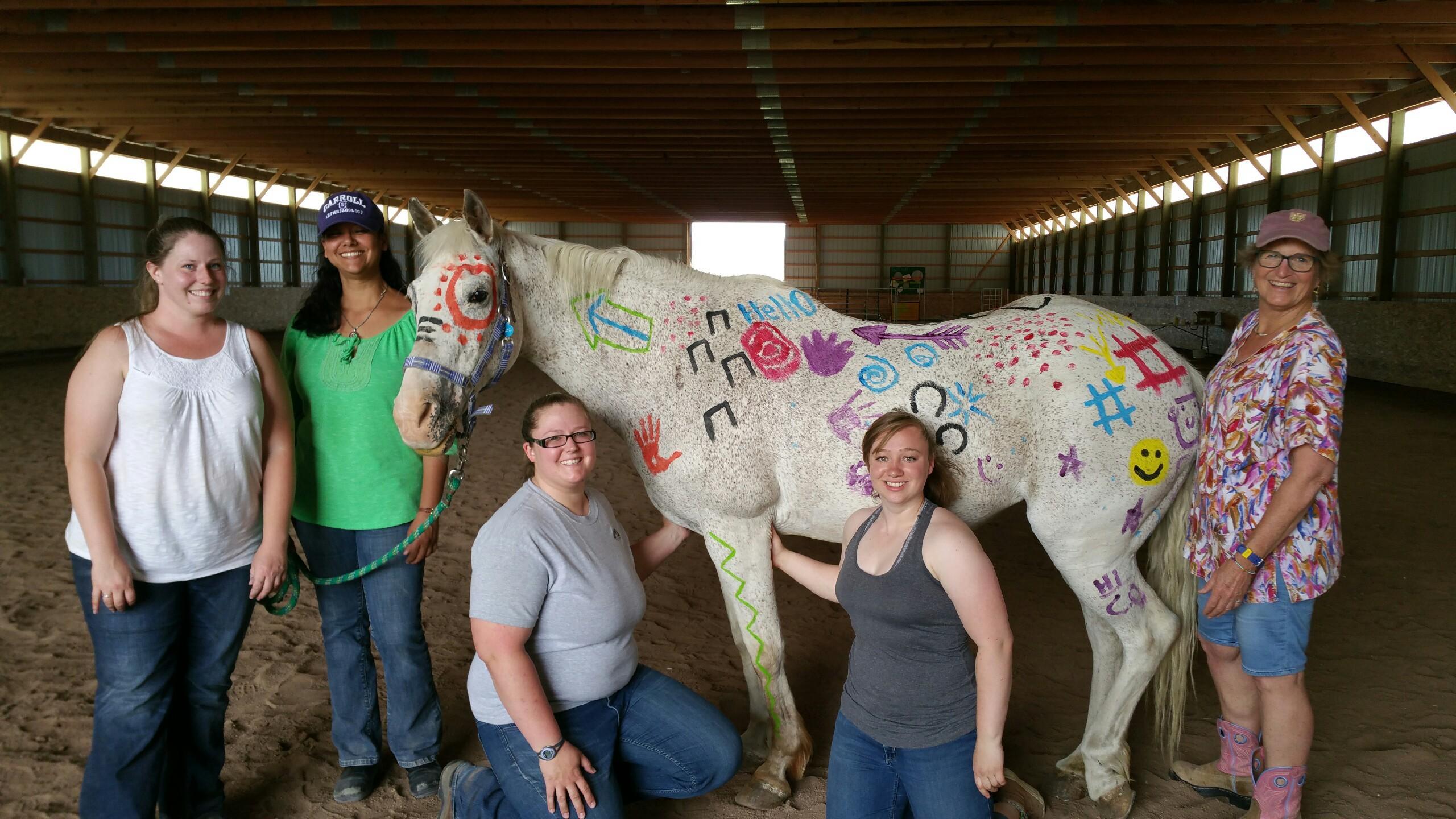 Students and Marie Suthers pose with a white horse in war paint