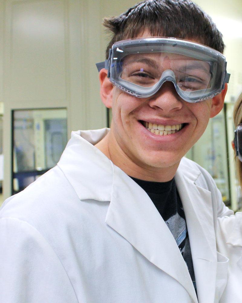 Matthew Rosman wearing a lab coat and safety goggles